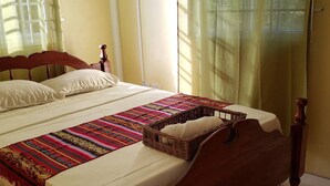 A bed with a wooden headboard, a colorful blanket, and a wicker basket with a pillow.