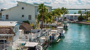 Uma marina com barcos atracados, um edifício branco com telhado de palha e palmeiras.