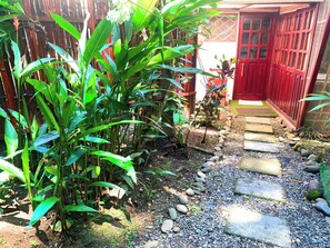 A garden pathway leading to a red door, surrounded by lush green plants and a wooden fence.