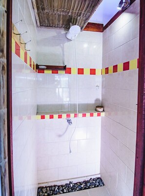 Shower area features a showerhead mounted on the ceiling, a hose, and two shelves with a basket.