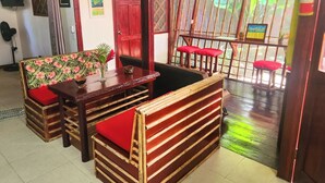 Una habitación con un banco de madera, una mesa con un jarrón de flores y vistas al exterior a través de una celosía de bambú.