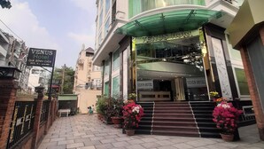 Entrada de hotel con toldo verde, escalones que conducen a la puerta y plantas en macetas.
