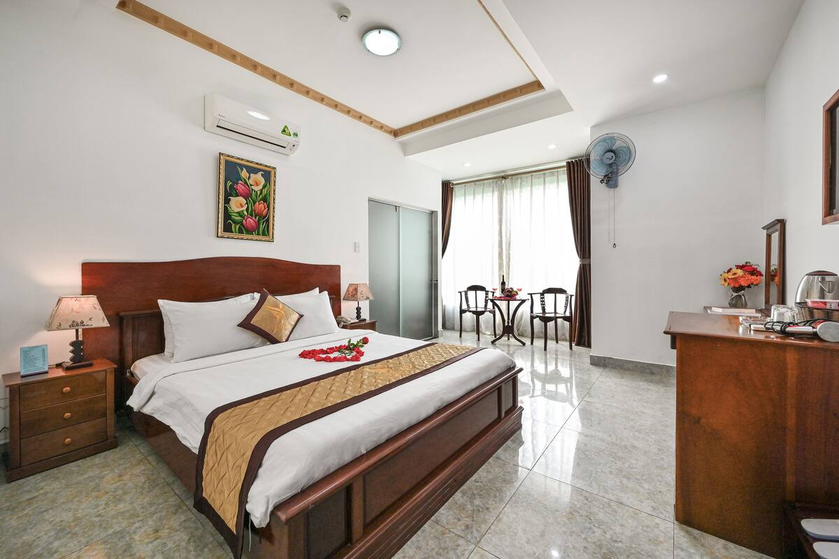 A hotel room with a large bed, bedside tables, a desk, and a dining area with chairs and a table.