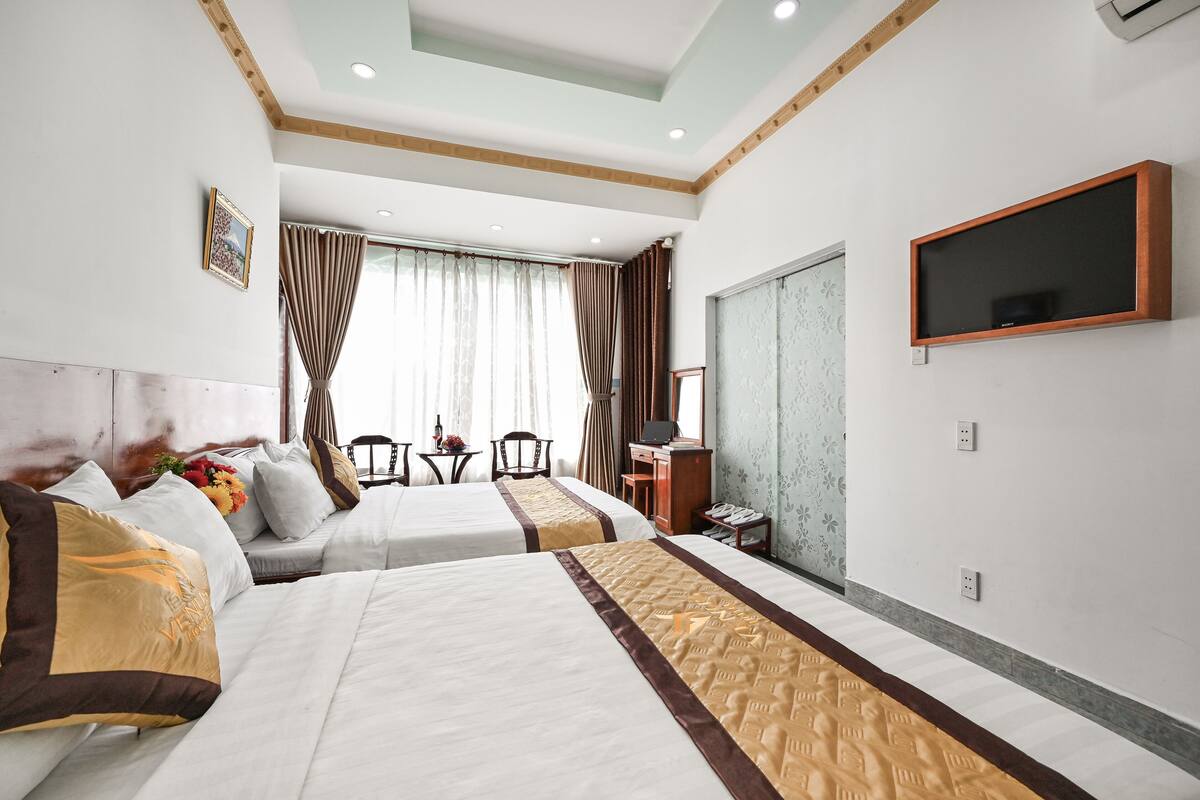 A hotel room with two beds, a desk, a chair, a TV, and a window with curtains.