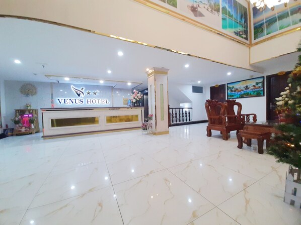 A hotel reception area with a marble floor, a reception desk, and a staircase leading to an upper level.