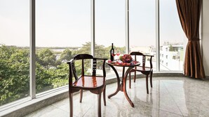 Un balcón con dos sillas de madera, una mesa con fruta y una copa de vino tinto, y vistas a zonas verdes y edificios.