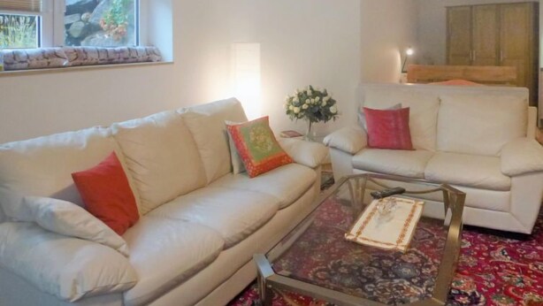 A living room with a beige sofa, a glass coffee table, and a red patterned rug.
