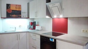 A modern kitchen with white cabinets, a built-in oven, a dishwasher, and a red accent wall.