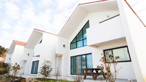 Une maison moderne à deux étages, dotée de grandes fenêtres, d’un toit recouvert de tuiles rouges et d’un petit jardin.