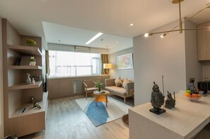 Una sala de estar moderna con un sofá, una mesa de centro y objetos decorativos. Se ve una ventana con cortinas, una lámpara y un estante en la pared con plantas.
