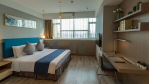 Habitación de hotel moderna con una cama grande, un escritorio y un televisor. Hay ventanas con cortinas, un cuadro en la pared y una estantería con plantas.