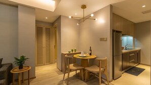 Una cocina moderna con horno integrado, refrigerador y lavaplatos. Hay un comedor con una mesa y sillas, y una pequeña planta sobre una mesita auxiliar.