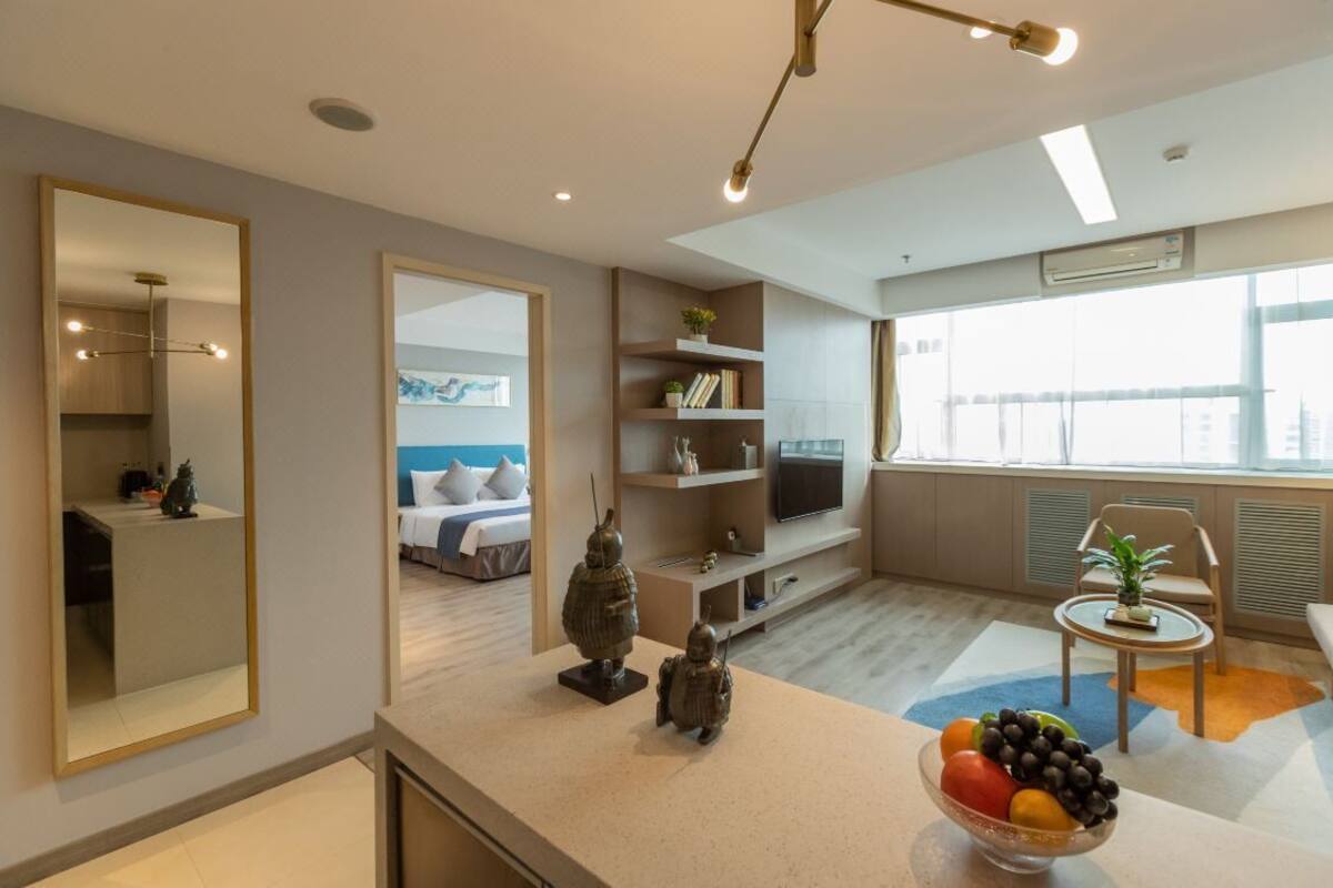 A modern hotel room with a bed, a TV, a small dining area, and a large window.