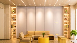 Un interior moderno con un sofá, sillas, una mesa redonda de madera y estanterías empotradas con plantas y libros.