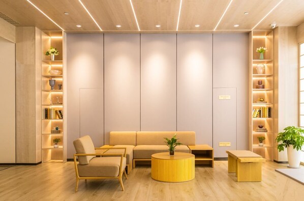 Un interior moderno con un sofá, sillas, una mesa redonda de madera y estanterías empotradas con plantas y libros.