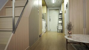 A modern kitchen with wooden cabinets, a built-in washing machine, and a small table with a vase. - Dongdaemun PR. Mondern Studio (Seoul)