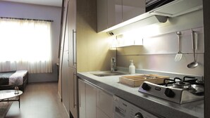 A compact kitchen with a gas stove, sink, and modern appliances. There is a dining area with a table and chairs, and a window with curtains. - Dongdaemun PR. Mondern Studio (Seoul)