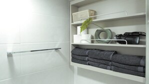 A bathroom with white tiles, a towel rack, shelves with towels, a plant, a toilet paper holder, and a camera. - Dongdaemun PR. Mondern Studio (Seoul)