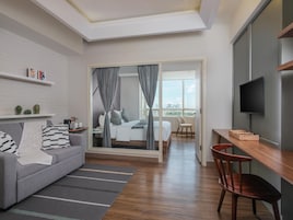 Habitación de hotel moderna con sofá, mesa de comedor, televisor y cama con vista a la ciudad.