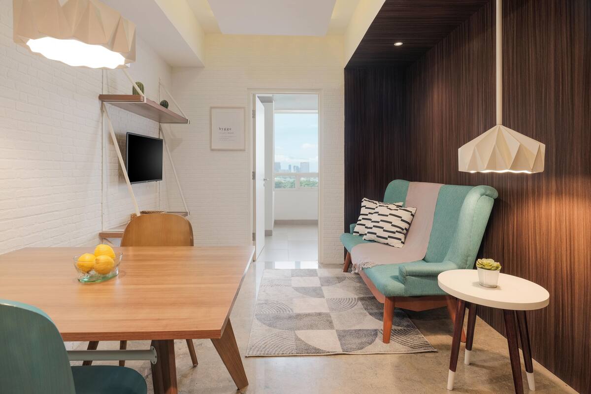 A modern living room with a wooden dining table, a green armchair, and a small white table.