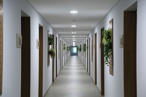 Ein langer, schmaler Korridor mit weißen Wänden, Holztüren und Deckenleuchten.