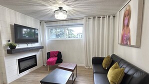 A living room with a fireplace, a television, a sofa, a coffee table, and a window with curtains.