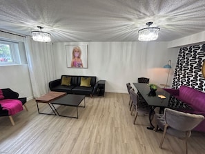 Una sala de estar moderna con un sofá negro, una mesa de centro de madera, una mesa de comedor con sillas y una araña.