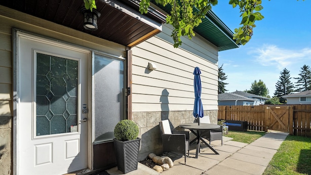 A house with a white door, a small patio with a table and chairs, and a wooden fence in the background.