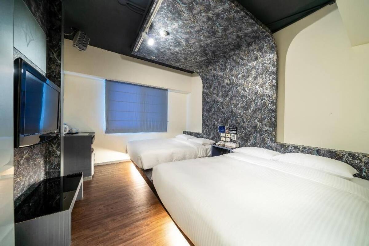 A hotel room with a modern design, featuring a large bed, a television, and a marble accent wall.