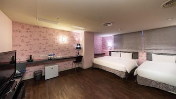 A hotel room with two beds, a desk with a chair, a small refrigerator, and a TV.