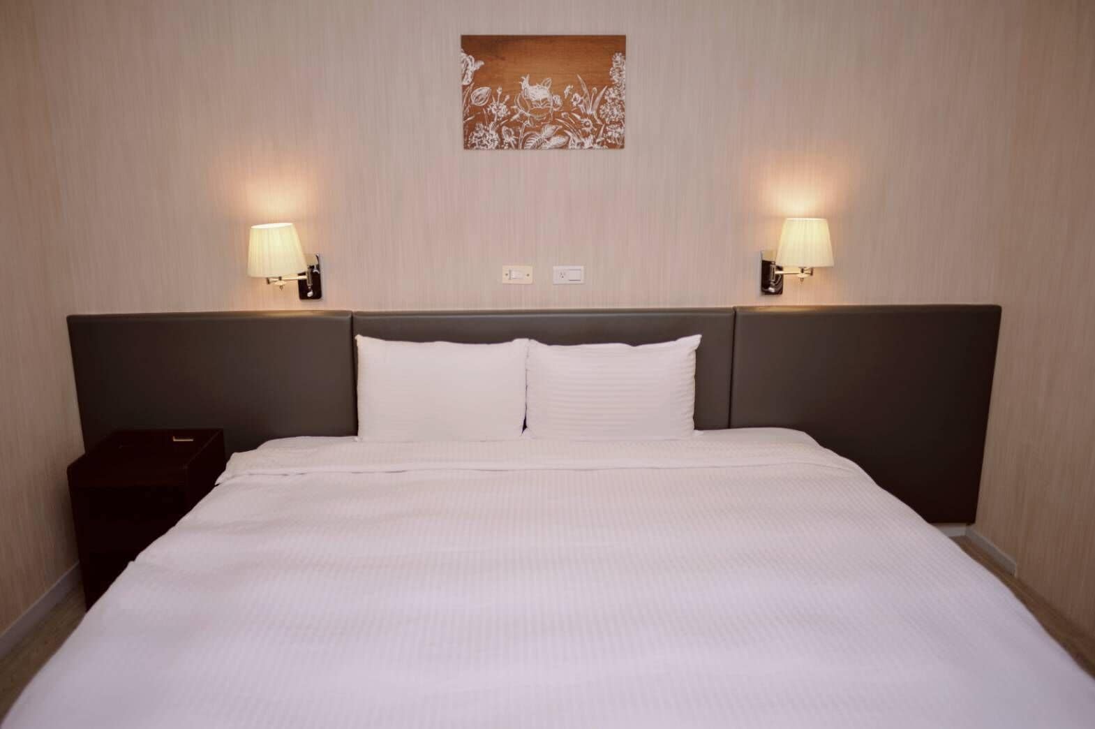 Hotellihuone, jossa on suuri sänky, kaksi yöpöytälamppua ja koristeellinen seinäkoriste.