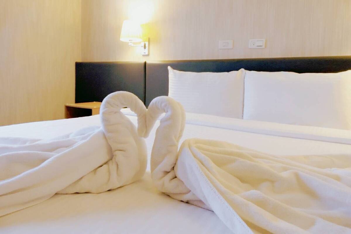 A hotel room with a neatly made bed, a bedside lamp, and a nightstand with a lamp.