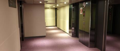 A hallway with carpeted floors, a sign indicating directions, and an elevator with a control panel.