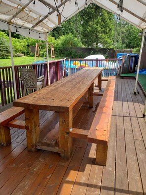 Eine Holzterrasse mit Picknicktisch und Bänken, umgeben von einer weißen Markise und Metallgeländern.