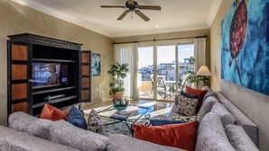 Un soggiorno con divano, televisore, ventilatore a soffitto e una grande finestra vista edifici.