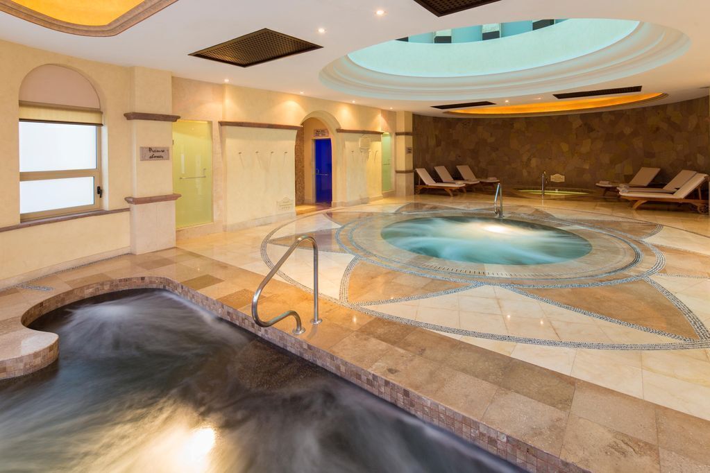 A spa area with a hot tub, lounge chairs, and a pool.