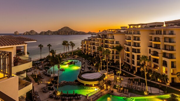 Un resort con piscina, palme e vista sul mare al tramonto.