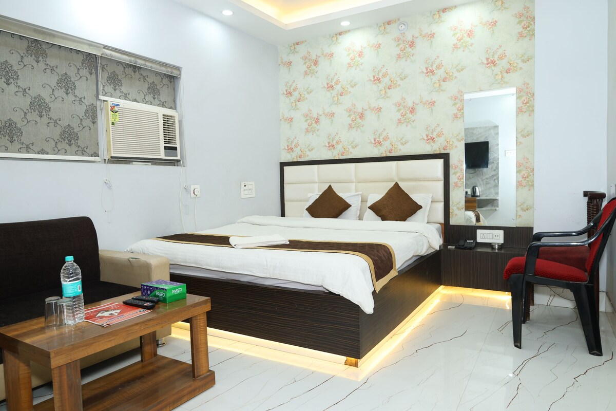 A hotel room with a bed, a desk, a chair, a window with an air conditioner, and a floral wallpaper.