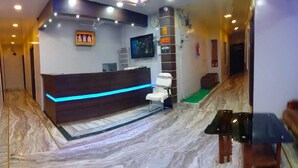 A reception area with a marble floor, a reception desk with a blue light, a white chair, and a television on the wall.