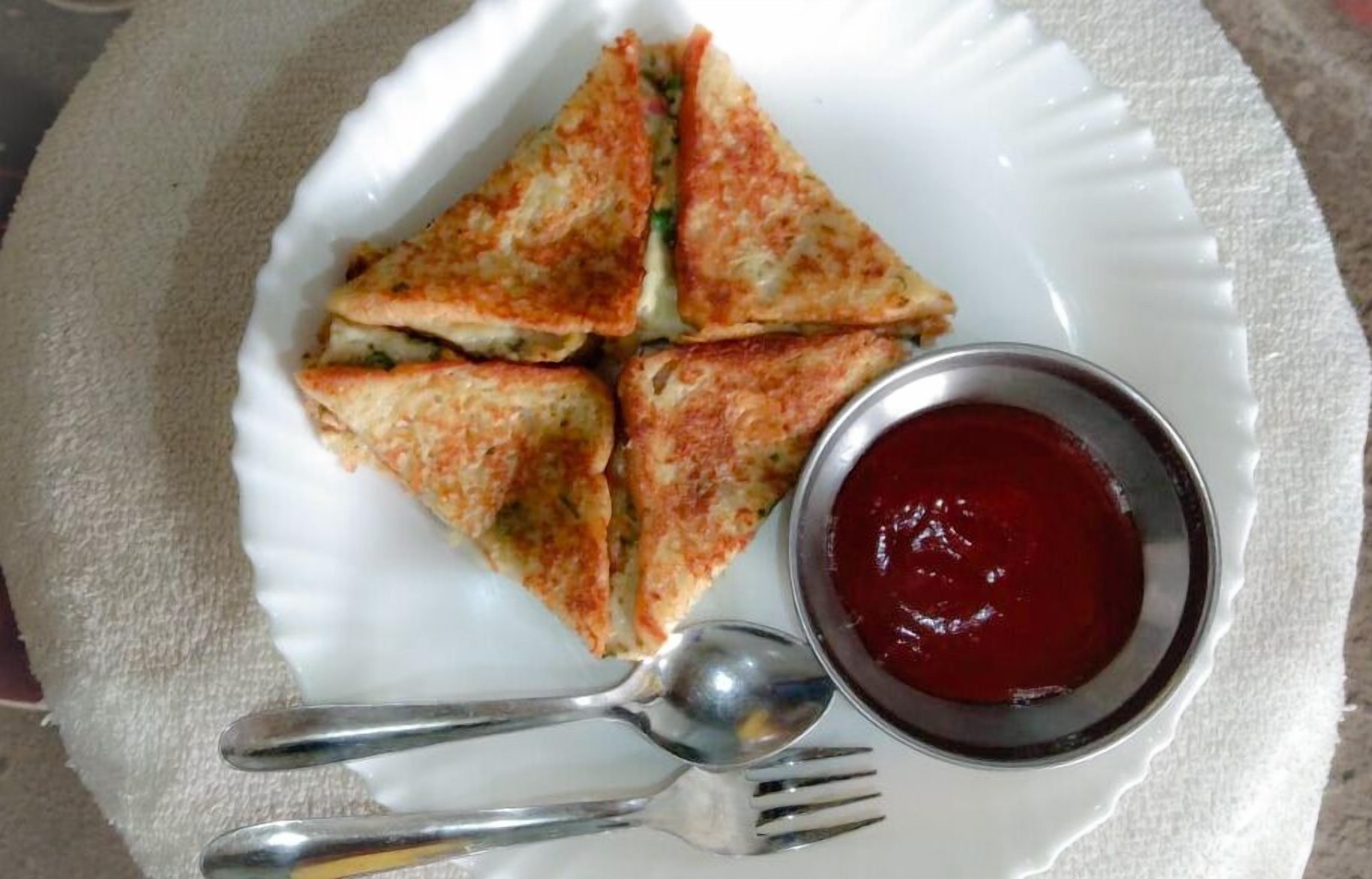 A plate with four triangular pieces of food and a small bowl of red sauce.