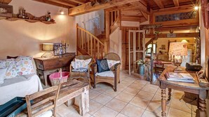 Un intérieur rustique en bois, avec un escalier, des meubles en osier et un coin cuisine visible à travers une porte ouverte.