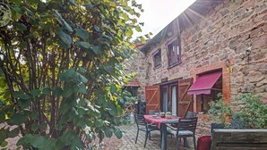 Un bâtiment en pierre avec une terrasse en briques, des meubles en bois et un auvent rouge.