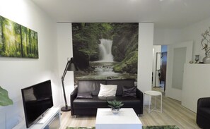 Relax in this stylish living room with a black leather sofa, flat-screen TV, and a beautiful forest waterfall mural.