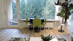 Un comedor con una mesa, sillas, una planta en maceta y vistas a árboles a través de amplias ventanas.