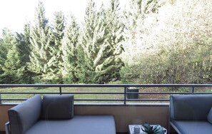 Un balcon avec un canapé gris et une petite table sur laquelle se trouvent une plante, une tasse et une pile d’assiettes.