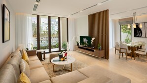A modern living room with a sofa, a coffee table, a TV, and a dining area with chairs and a table. - Oakwood Ha Long (Bai Chay)