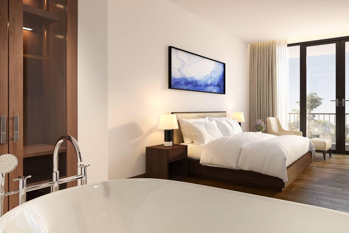 Habitación de hotel con una cama grande, una bañera, un escritorio con silla y vistas al exterior.