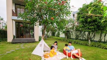 A family picnic in a garden with a tent, grass, and a building in the background.