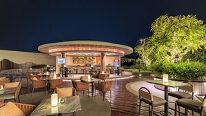 An outdoor dining area with round tables and chairs, a bar with a Coca-Cola sign, and a large illuminated tree. - Oakwood Ha Long (Bai Chay)