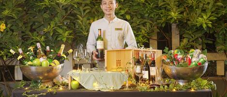 A table set with bottles of wine and cans, surrounded by greenery.